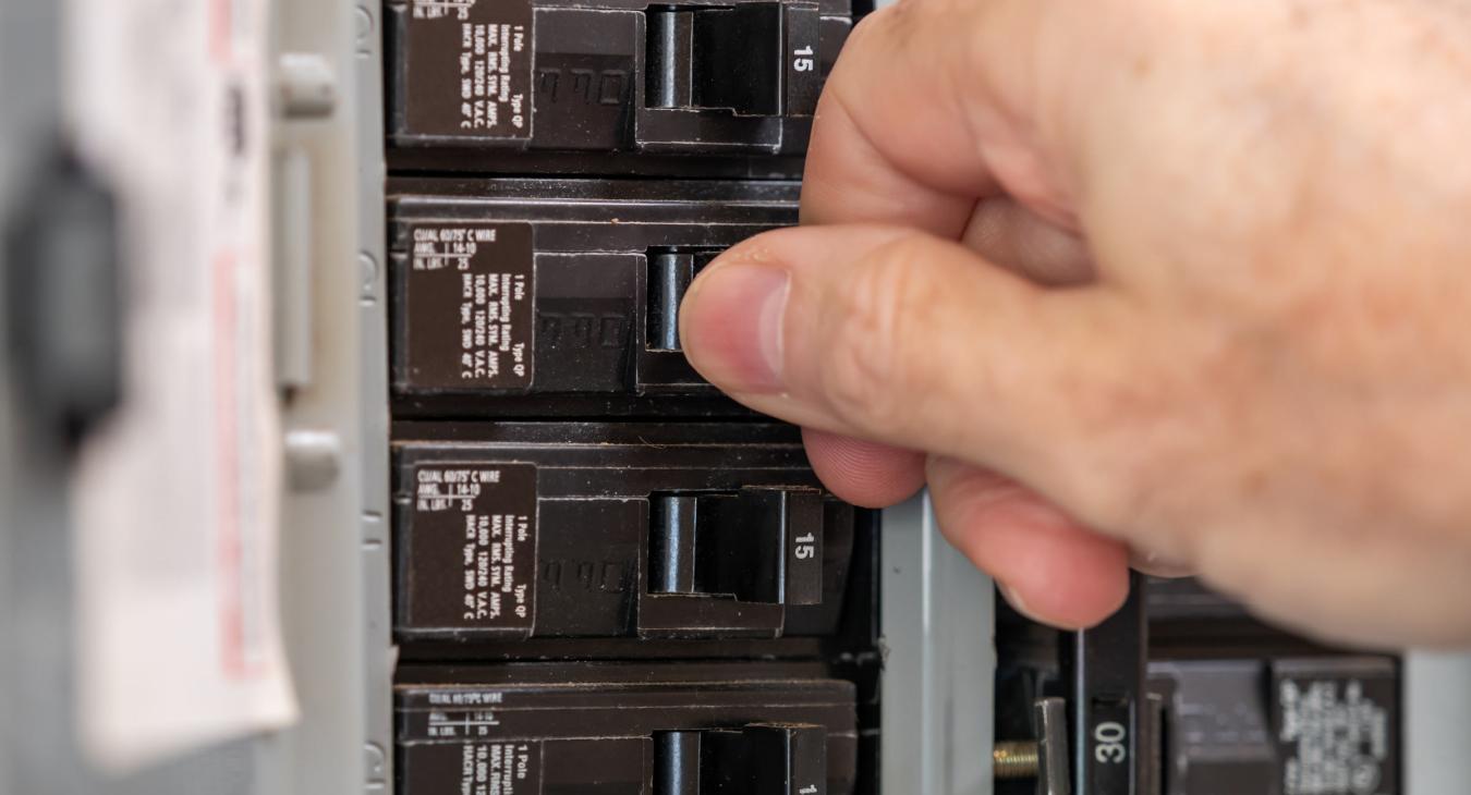 A hand flips a breaker in an electrical service box